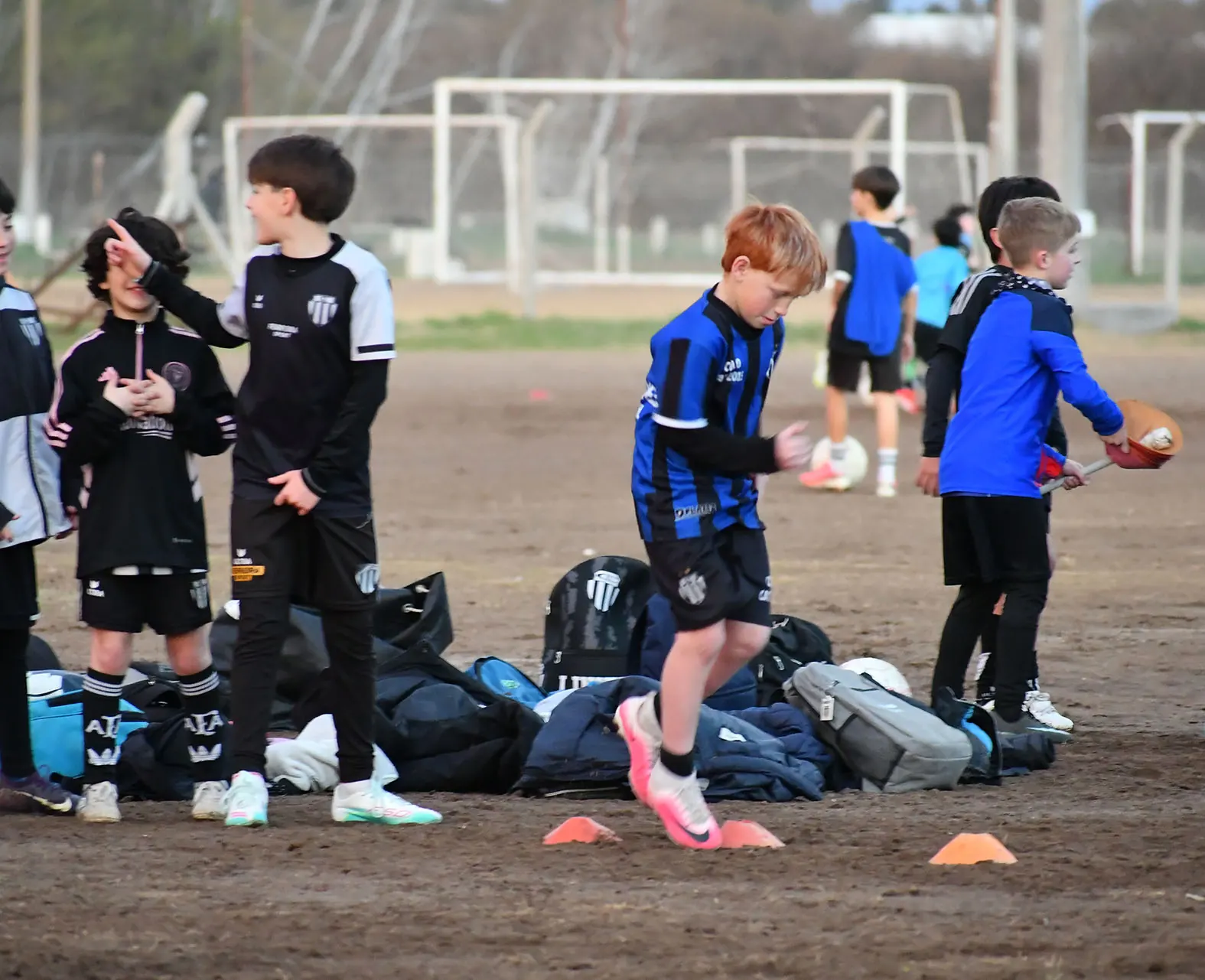 Chicos de las inferiores de Liniers en pleno entrenamiento sobre una cancha de tierra, con los arcos de fondo