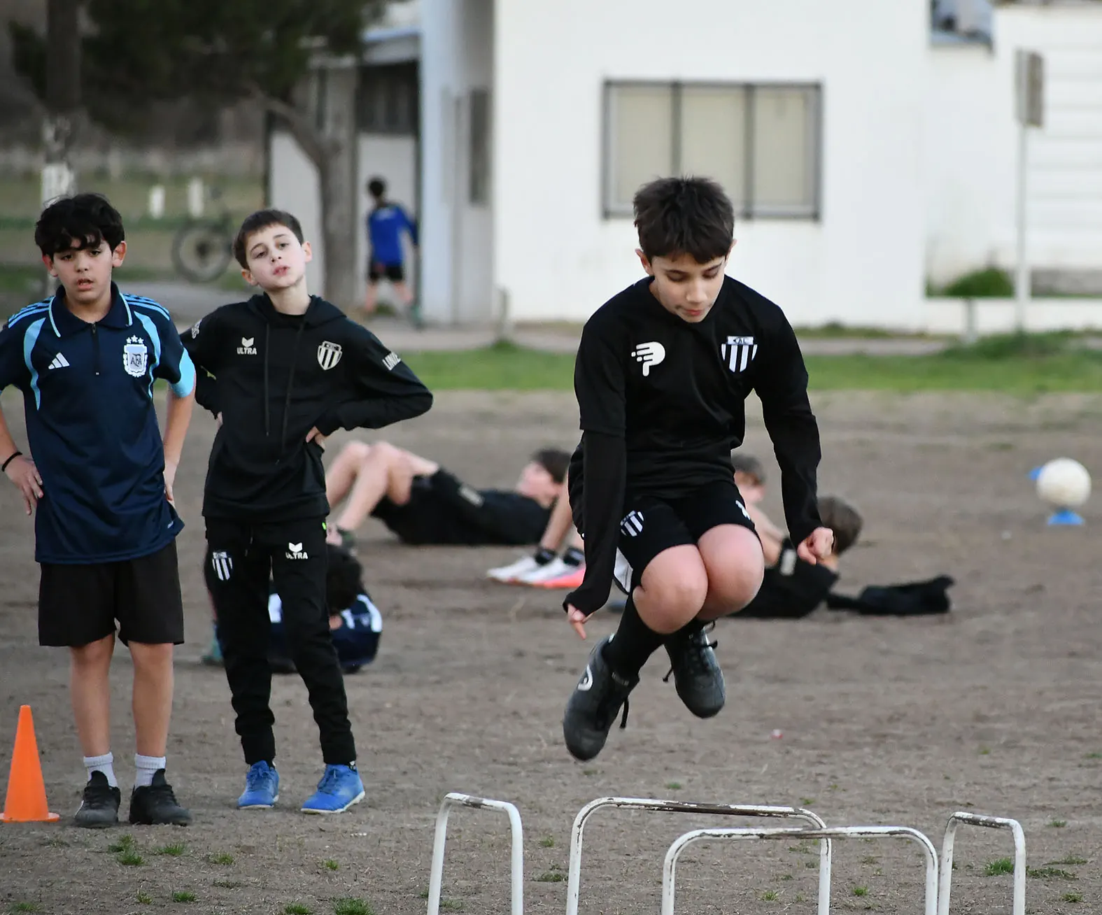 Un chico de las inferiores de Liniers salta una valla durante un entrenamiento mientras sus compañeros esperan su turno